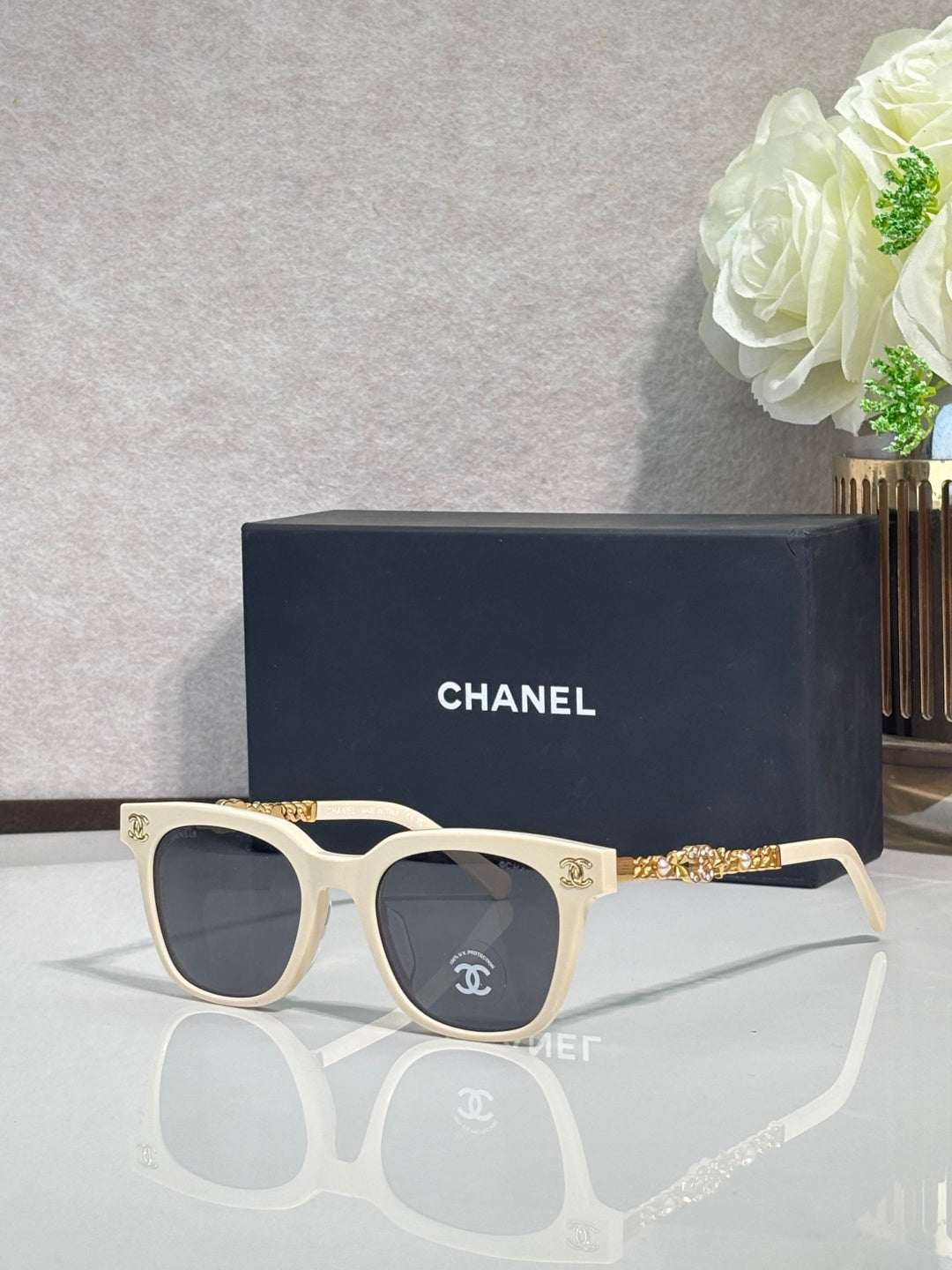 Sunglasses with cream frames, gold chain detail on temples, and dark lenses