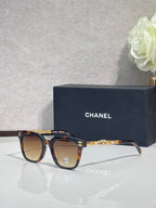 Sunglasses with tortoiseshell frames, gold chain temple detail, and dark lenses