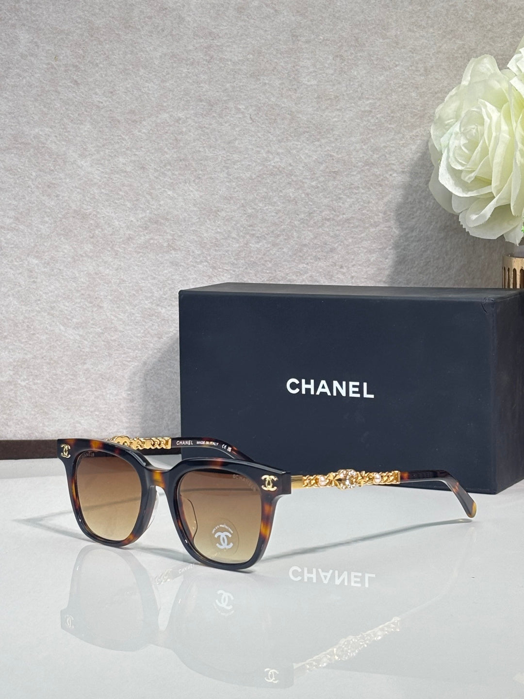Sunglasses with tortoiseshell frames, gold chain temple detail, and dark lenses