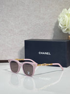Sunglasses with pink frames, gold chain temple detail, and dark lenses