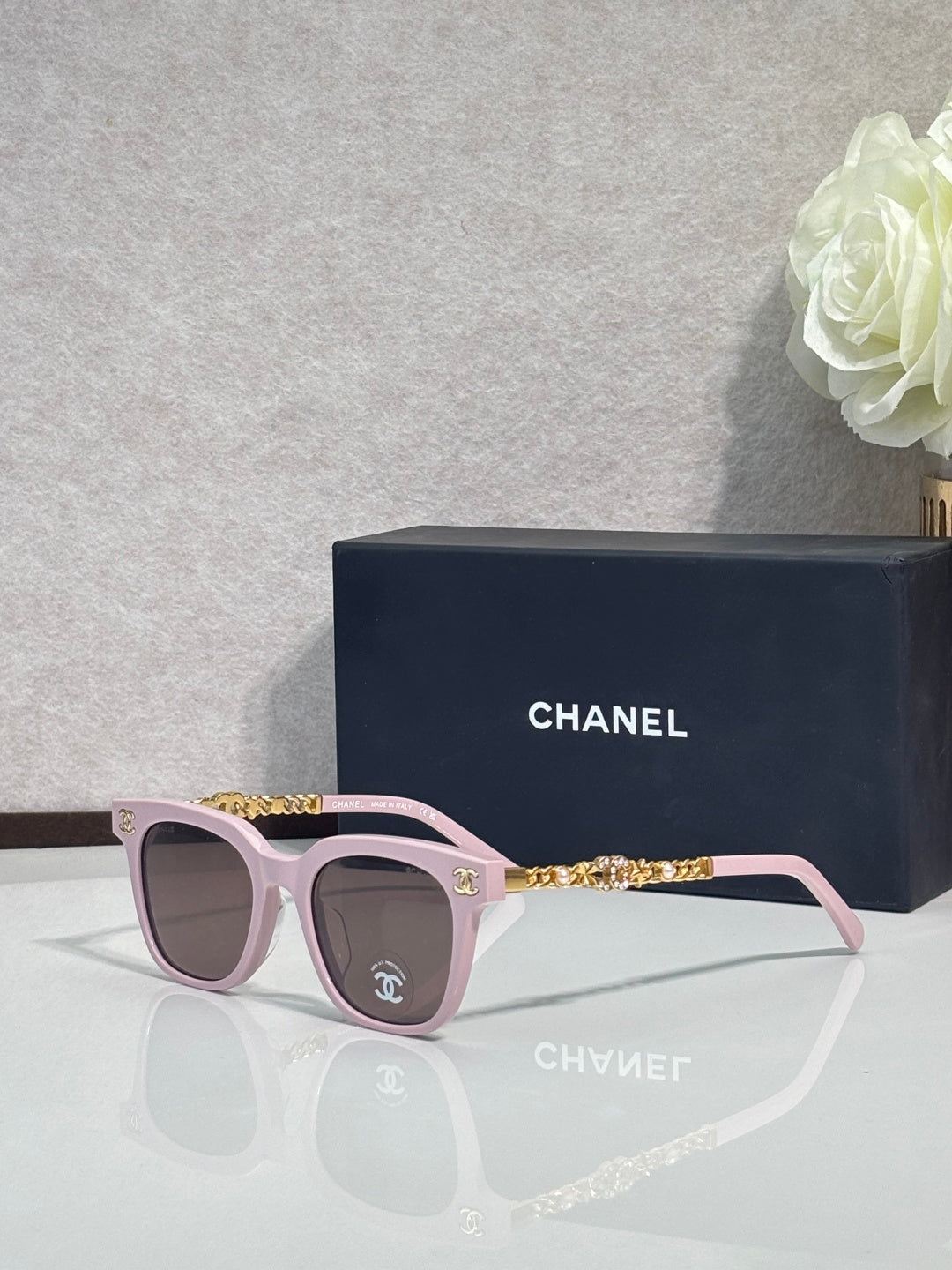 Sunglasses with pink frames, gold chain temple detail, and dark lenses