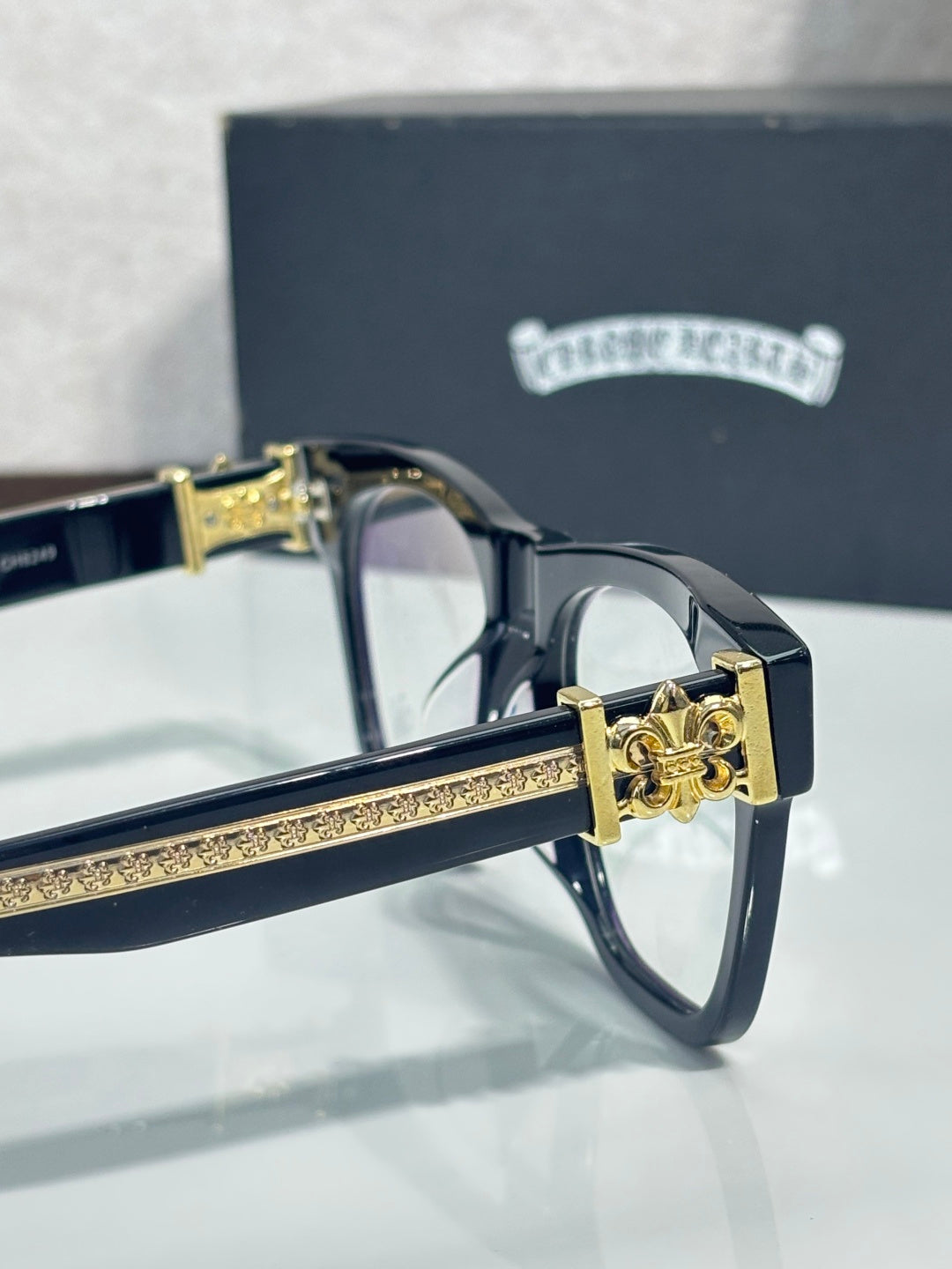 Chrome glasses with gold-tone hinge and dark frame temple, ornate crest detail