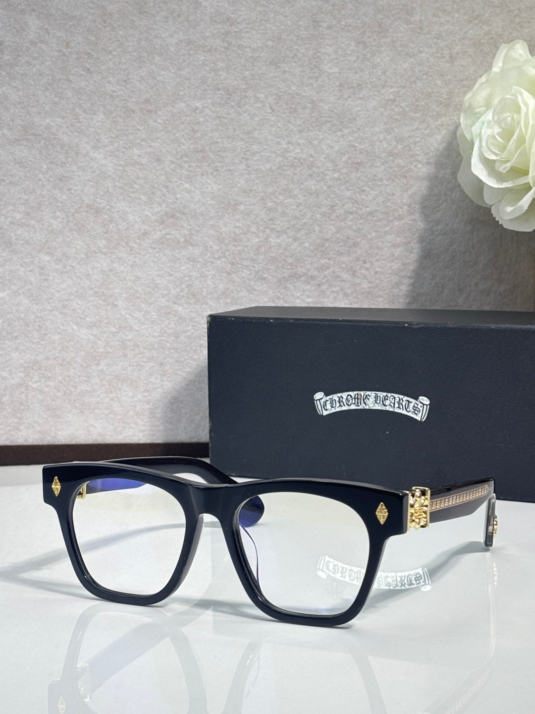 Chrome glasses with dark frames and gold-tone side emblem accents