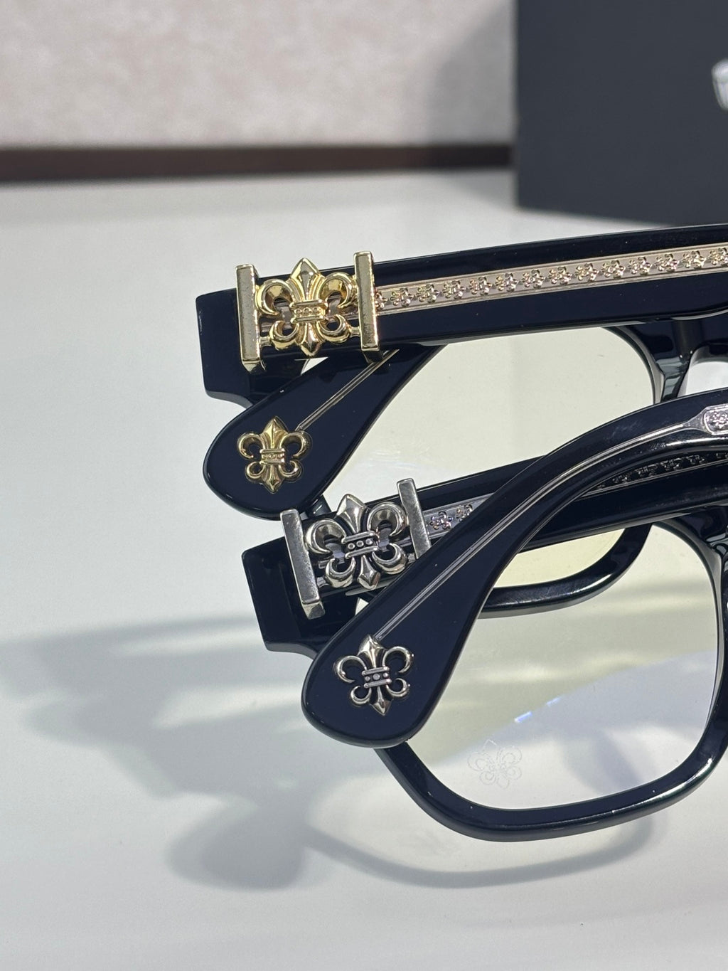 Chrome glasses with navy frames and gold-tone fleur-de-lis hinge ornament close-up