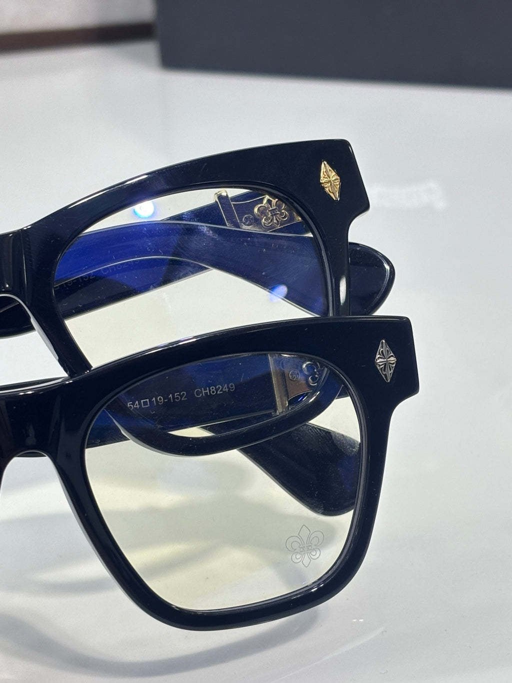 Chrome glasses with navy blue square frames and small gold fleur-de-lis emblems