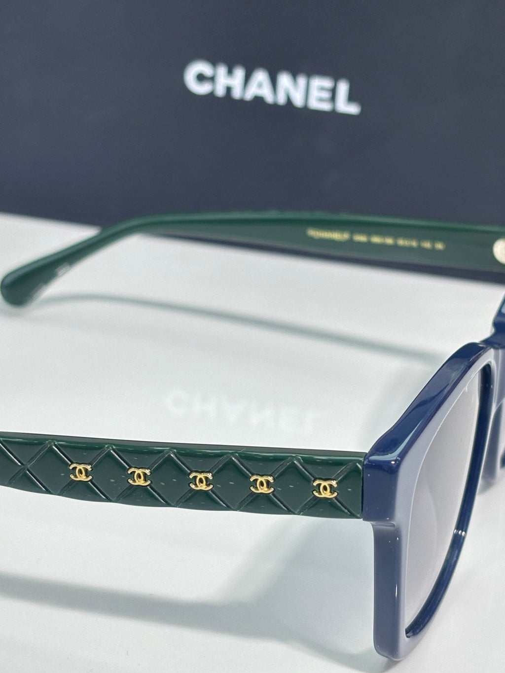 Green patterned temple sunglasses with blue arms and dark tinted lenses, logo detail