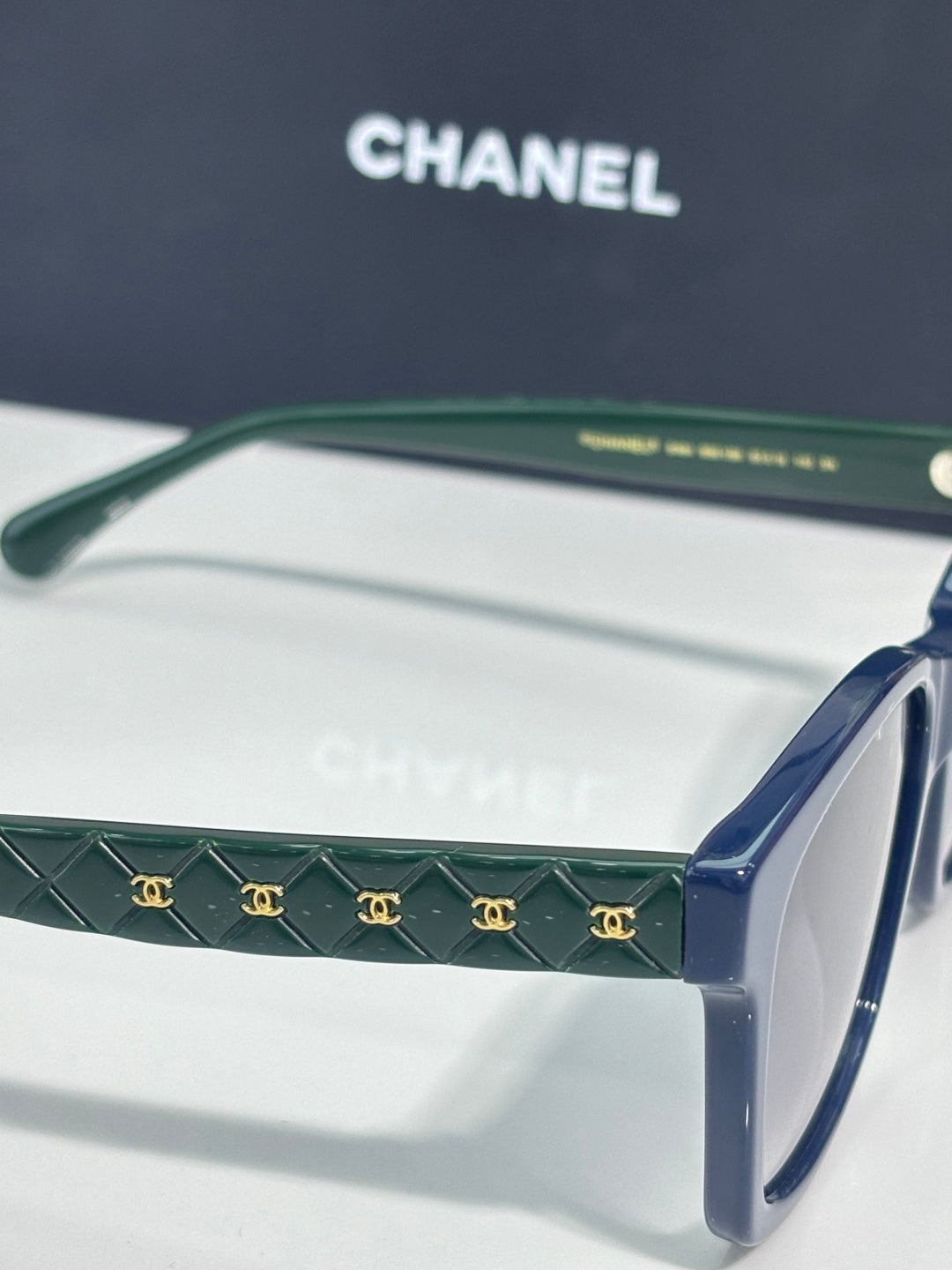 Green patterned temple sunglasses with blue arms and dark tinted lenses, logo detail