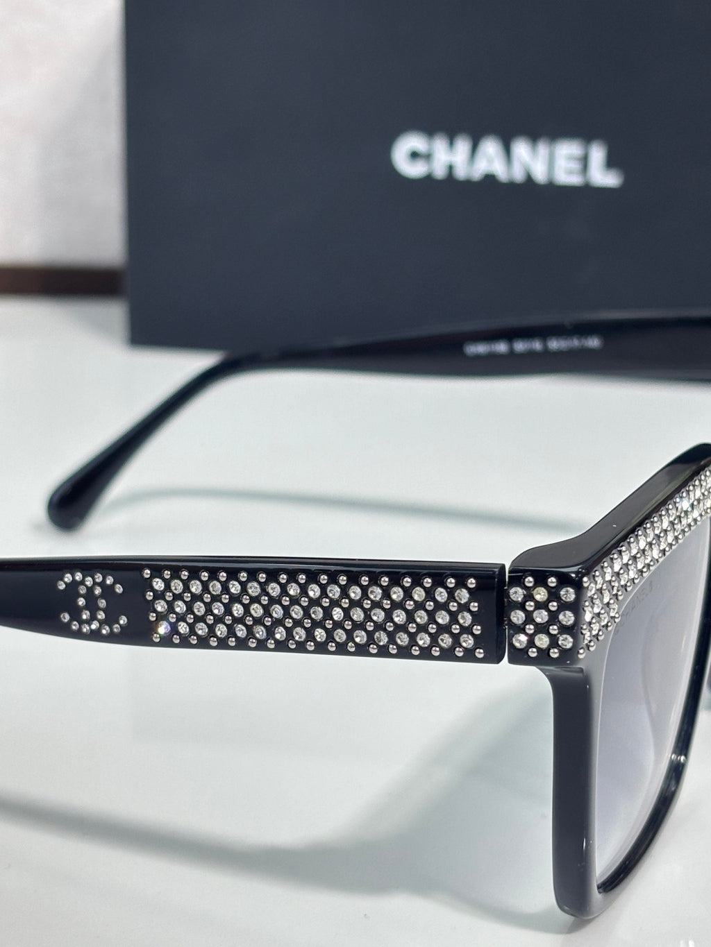 Chanel sunglasses with black frame and silver rhinestone pattern on front bar