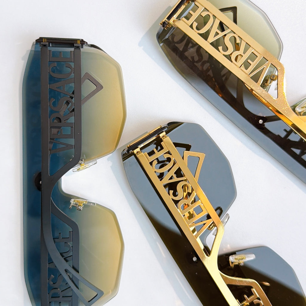 Gold sunglasses close-up with blue tint lenses and ornate Versace logo side panels