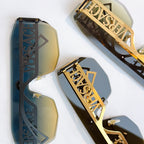 Gold sunglasses close-up with blue tint lenses and ornate Versace logo side panels