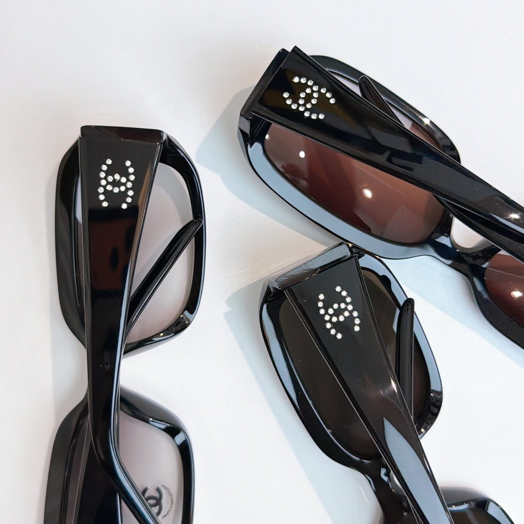 Black glasses set shown in close-up with rhinestone logo accents
