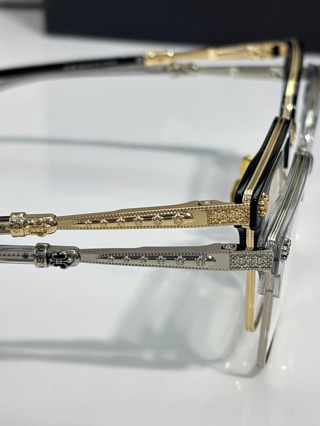 Close-up metal eyeglass hinge and gold-toned temple with engraved pattern