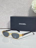 Oval sunglasses with gold frame, dark lenses, and ornate gold front detail