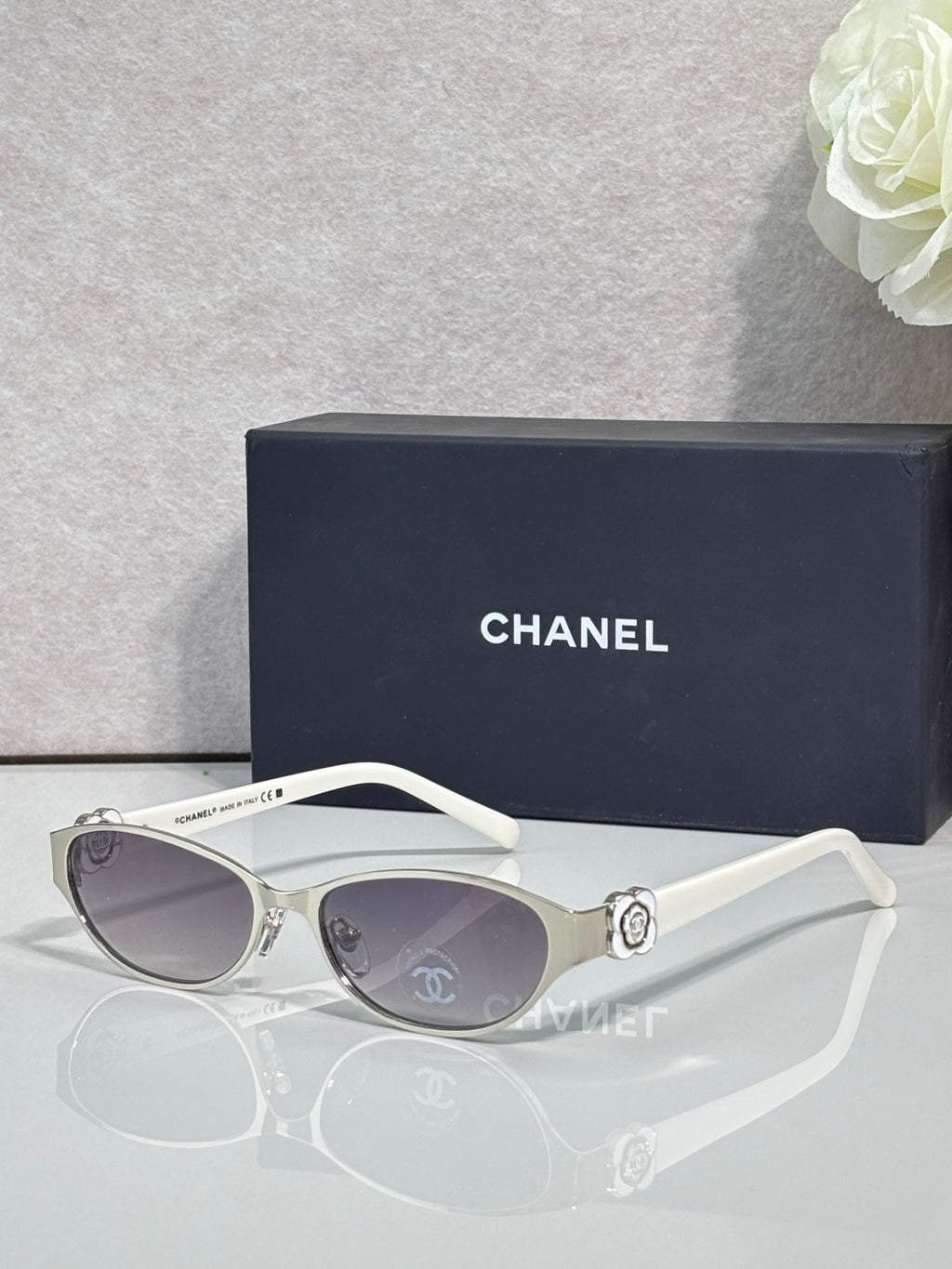 Oval sunglasses with white frame, light lenses, and silver flower hinge