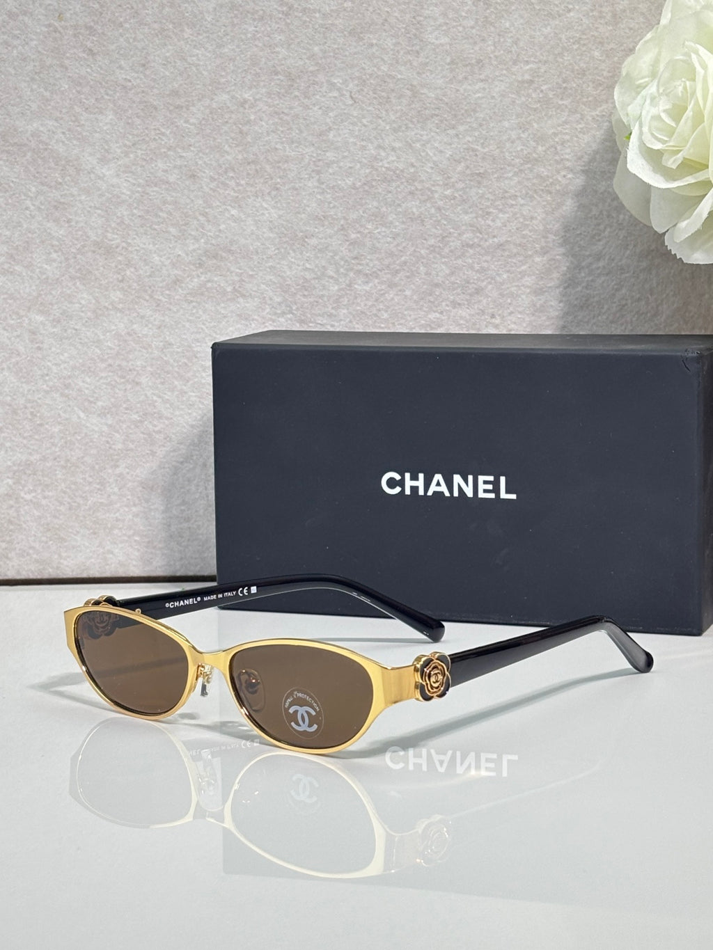 Oval sunglasses with gold frame, dark lenses, and black temple tips