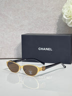 Oval sunglasses with gold frame, dark lenses, and black temple tips