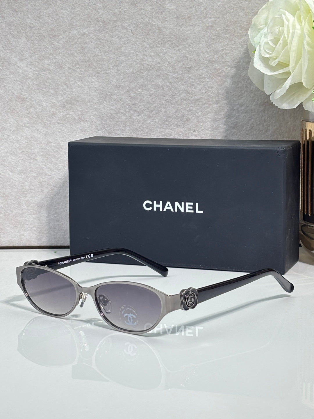 Oval sunglasses with silver frame, dark lenses, and black temple accents