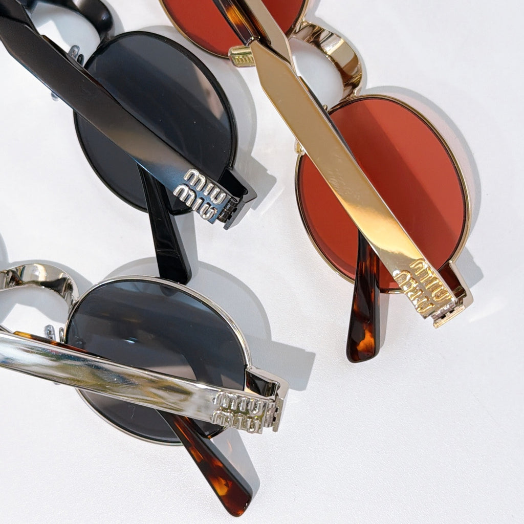 MiuMiu round sunglasses close-up with black and gold frames and dark lenses