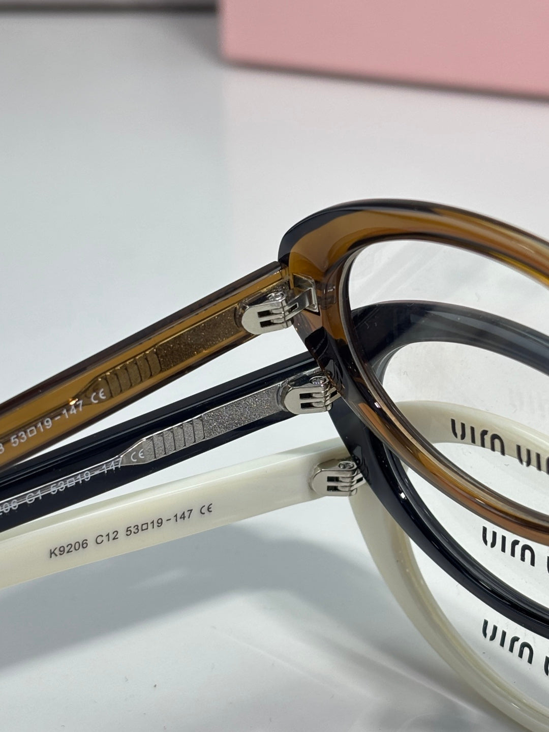 Eyeglasses close-up: tortoiseshell and cream frames with metal hinge and temple detail.