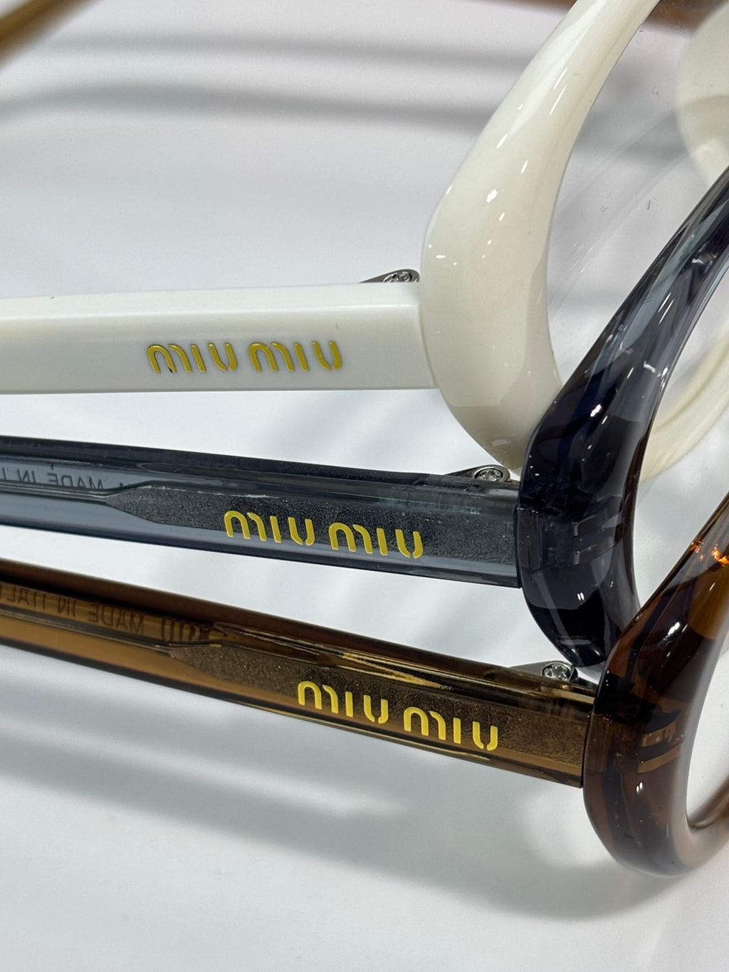 Cream and black eyeglasses stacked, visible temple text and glossy frames.