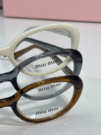 Cream and dark eyeglasses stacked, close-up of rounded frames and temple logos.