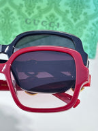 Gucci sunglasses close-up with red frame, dark lenses, and gold hardware