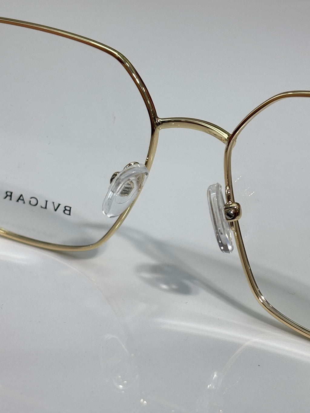 Gold metal eyeglasses with clear lenses and engraved logo on temple, close-up view.