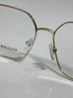 Gold metal eyeglasses with clear lenses and engraved logo on temple, close-up view.