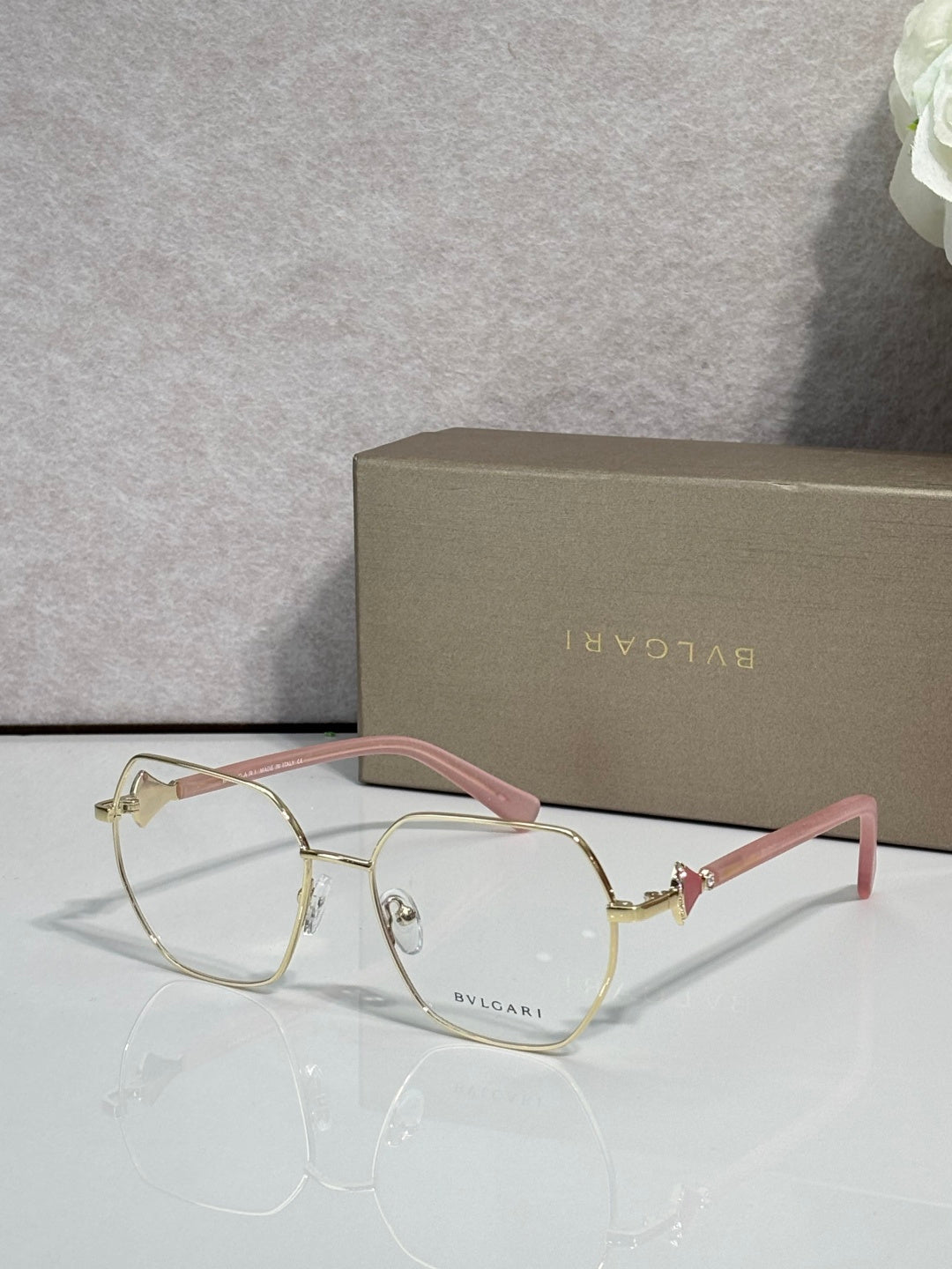 Gold metal round eyeglasses with clear lenses and pink-tinted temple accents, logo.