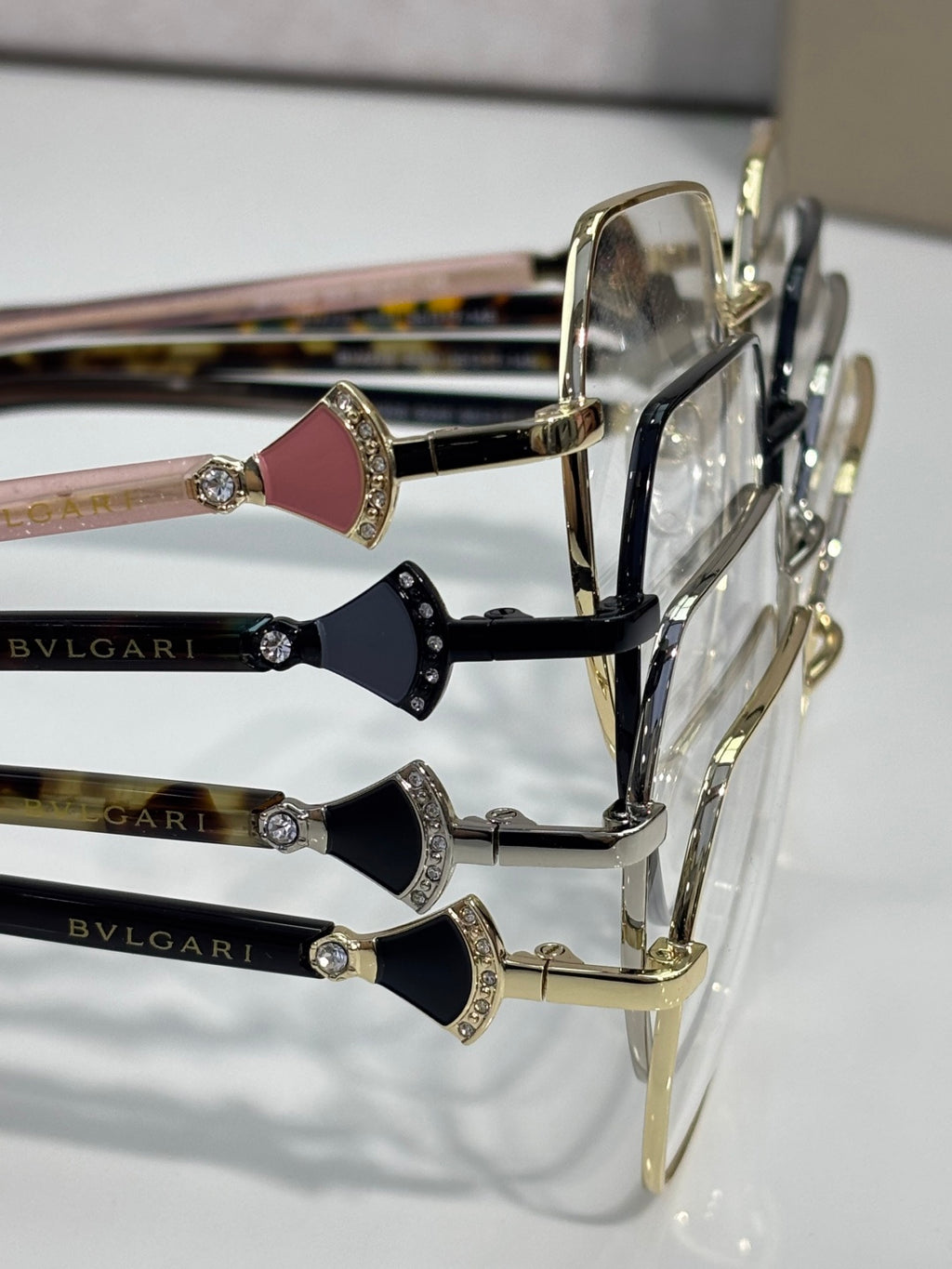 Assorted eyeglass frames with gold rims and gem details on temple fronts, logo.
