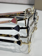Assorted eyeglass frames with gold rims and gem details on temple fronts, logo.