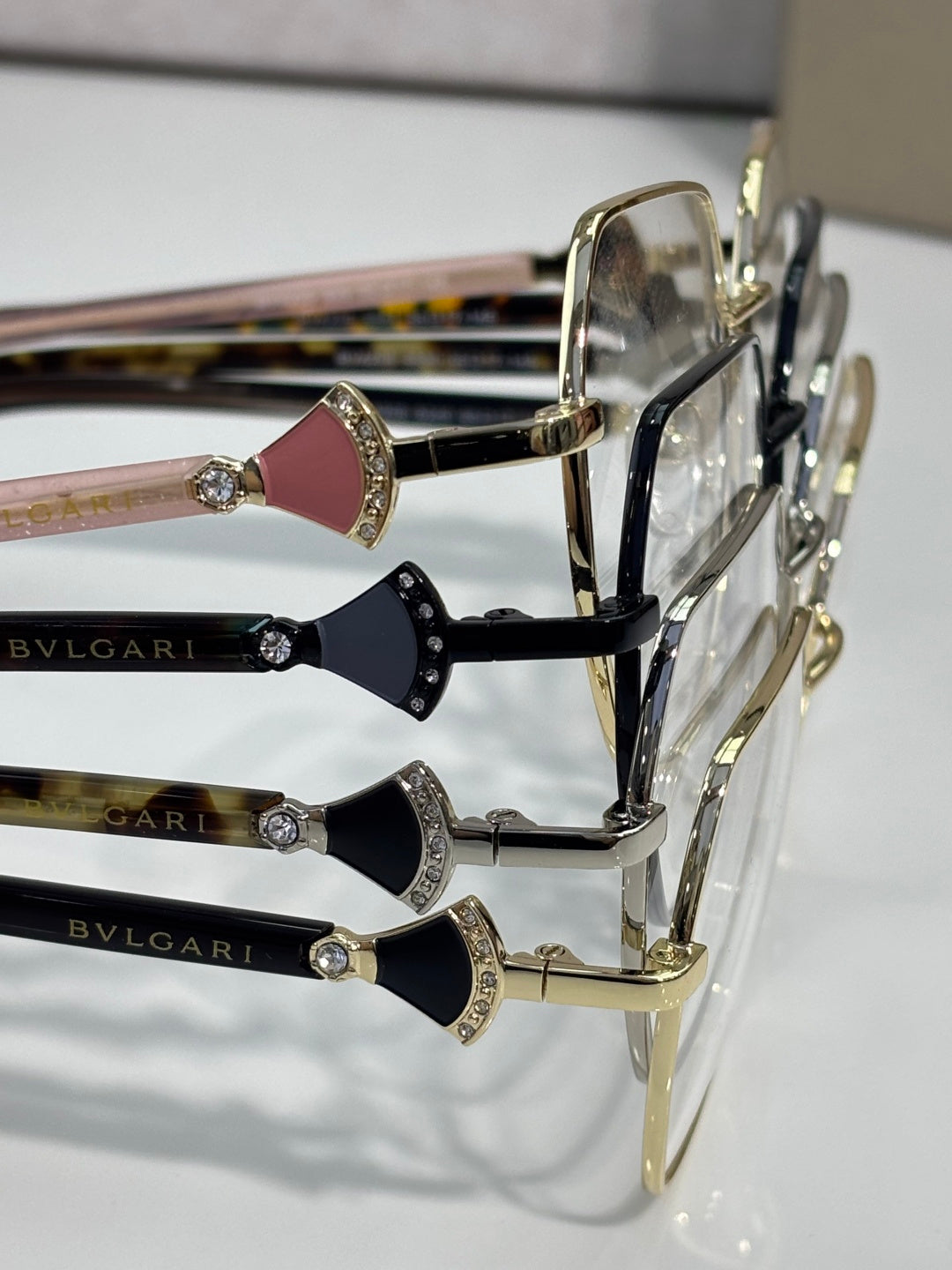 Assorted eyeglass frames with gold rims and gem details on temple fronts, logo.