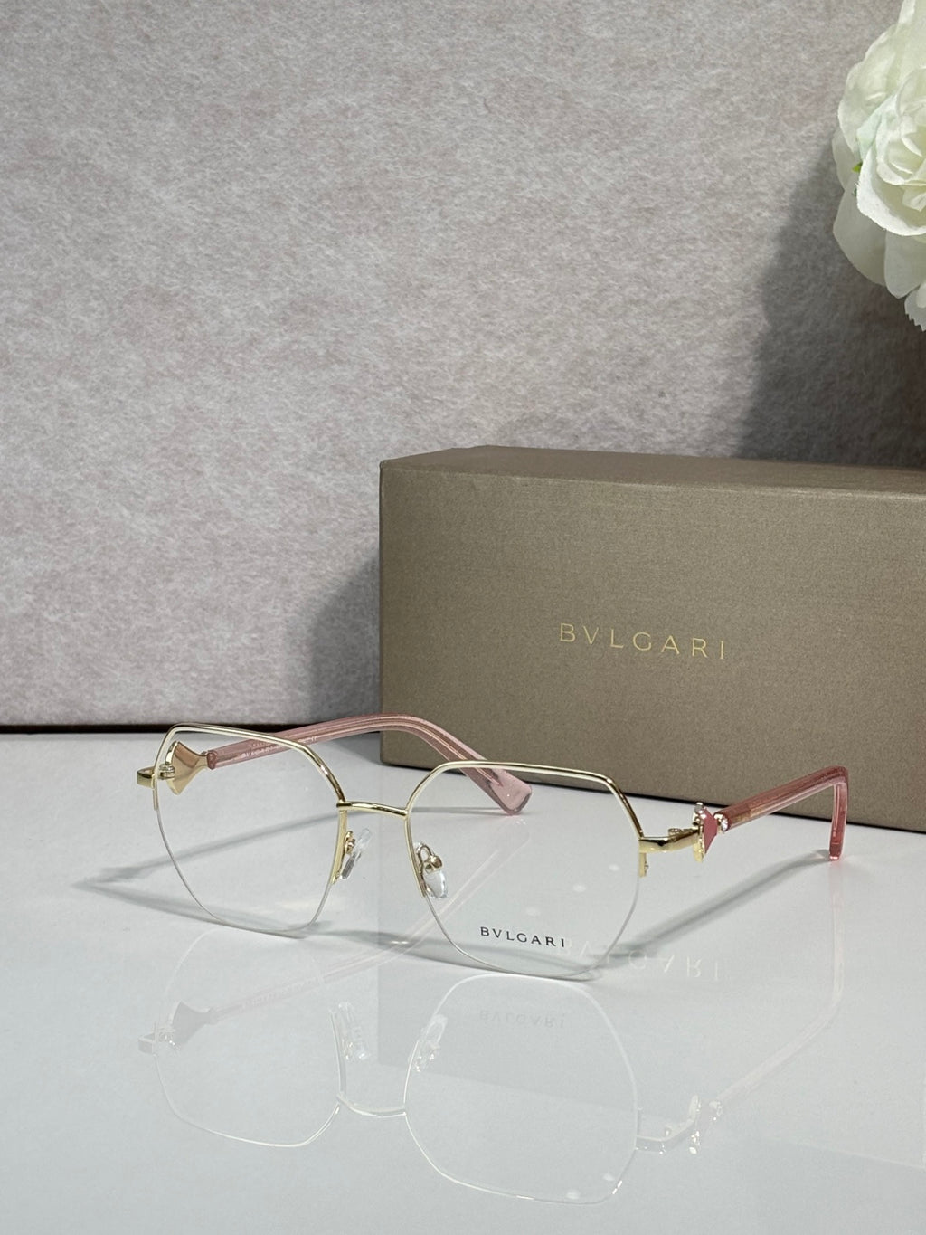 Eyeglasses with clear lenses and gold-tone metal frame, pale pink temple accents.