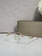 Eyeglasses with clear lenses and gold-tone metal frame, pale pink temple accents.