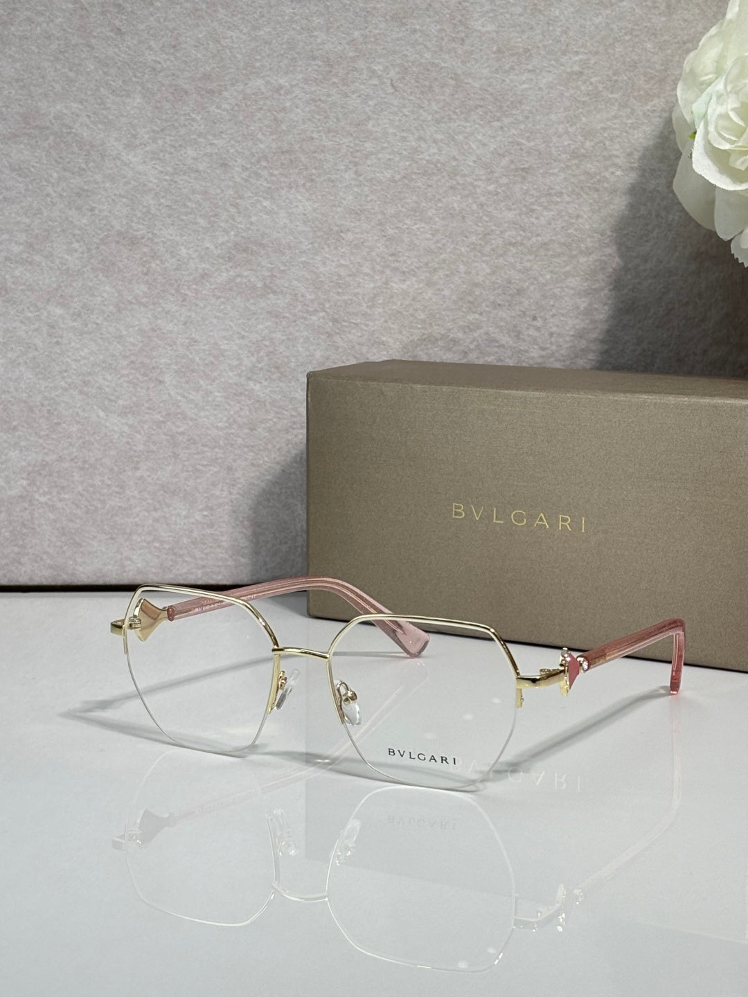 Eyeglasses with clear lenses and gold-tone metal frame, pale pink temple accents.