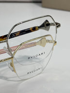 Eyeglasses close-up: tortoiseshell temple with pink accent, gold-tone metal frame.