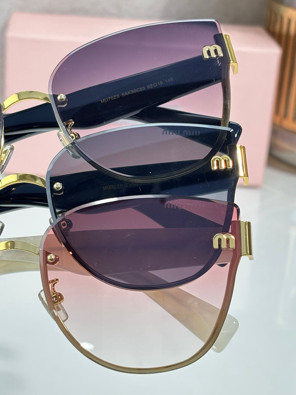 Purple gradient round sunglasses with gold-tone frames stacked on a pink box