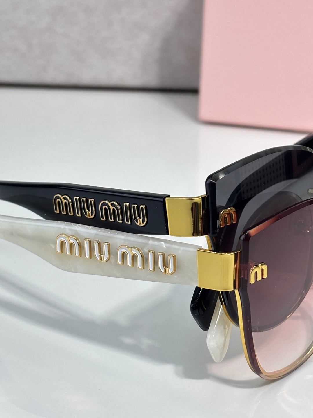 Black glasses temples with “miu miu” logo band and gold hinge, gradient lenses