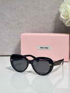 MiuMiu black round sunglasses with gold logo temples and dark gradient lenses