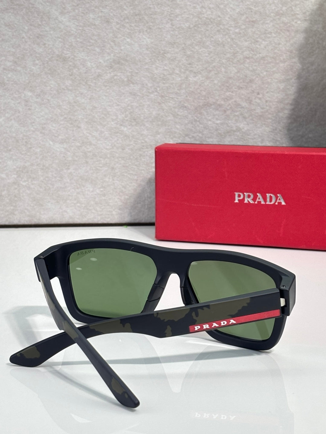 Black camo sunglasses with green lenses and angled side view, Prada logo.