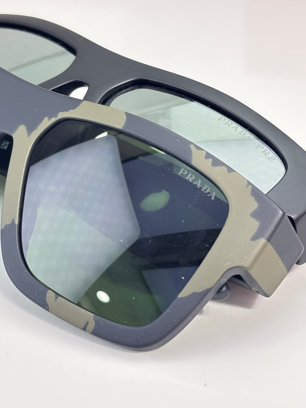 Oversized camo sunglasses close-up with dark green lenses and Prada branding.