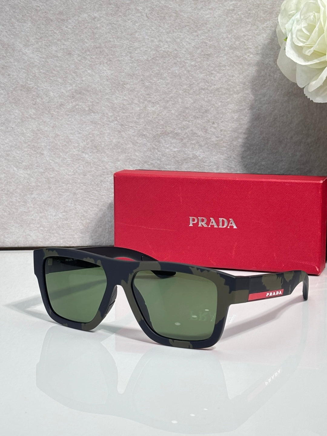 Dark blue camo sunglasses with green lenses and red Prada logo stripe.