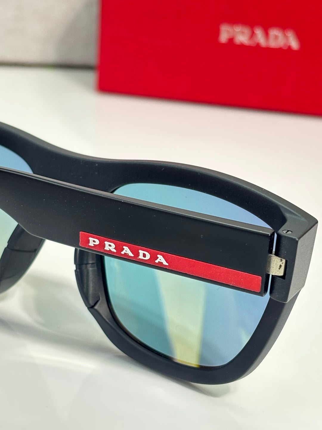 Prada sunglasses close-up: black frame with red PRADA logo on bridge