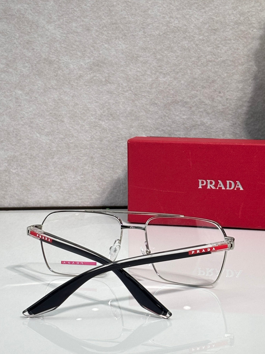 Prada eyeglasses with clear lenses and slim metal frame, black temple arms with logo.