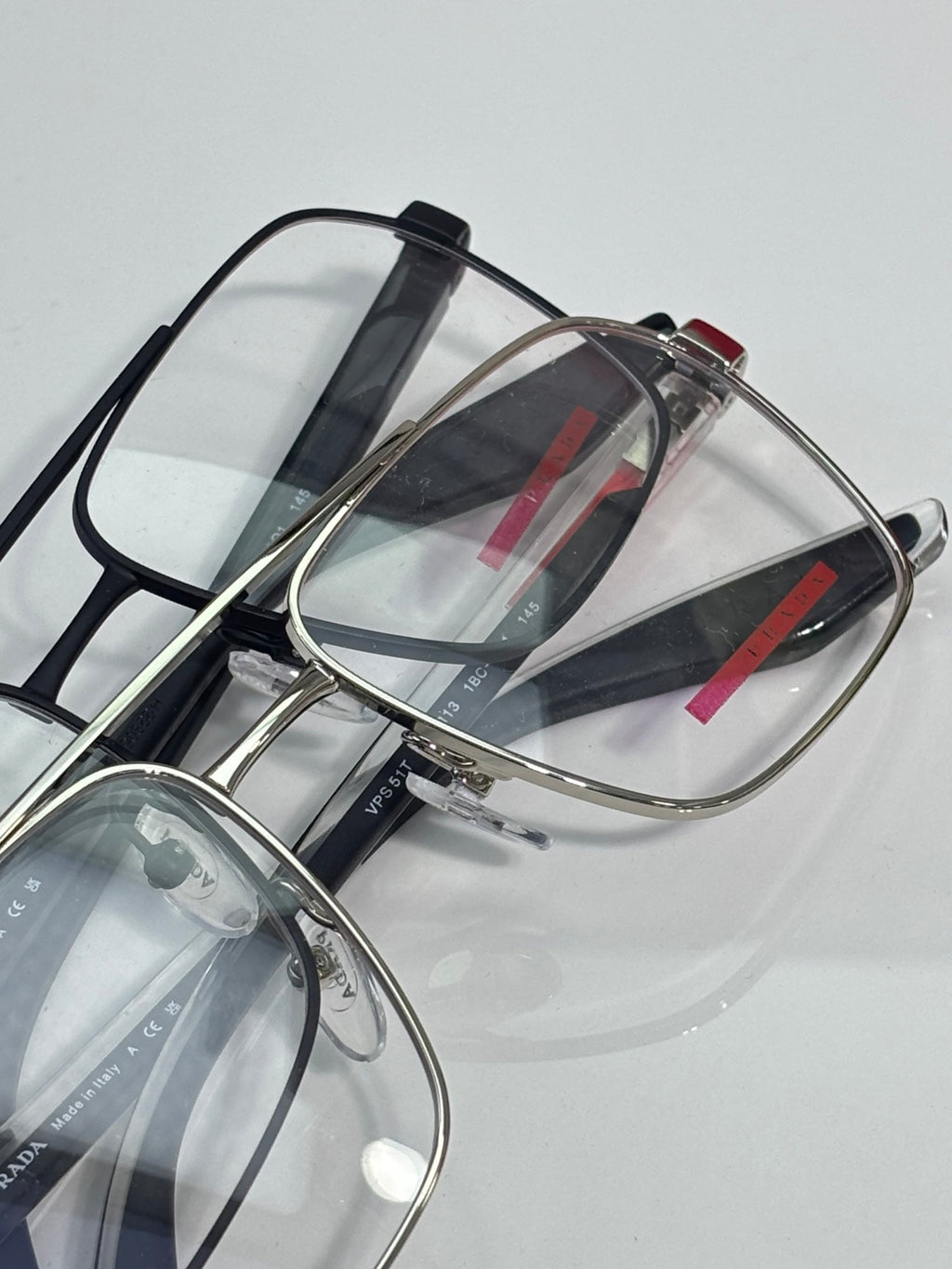 Prada eyeglasses with clear lenses and metal frame, red logo stripe on black temple.