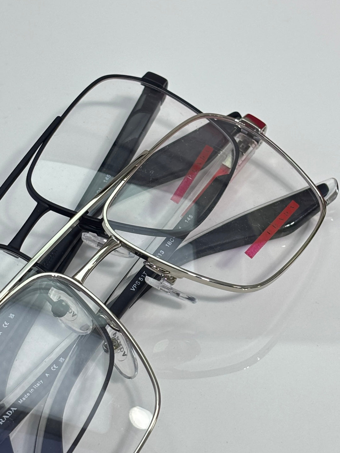 Prada eyeglasses with clear lenses and metal frame, red logo stripe on black temple.