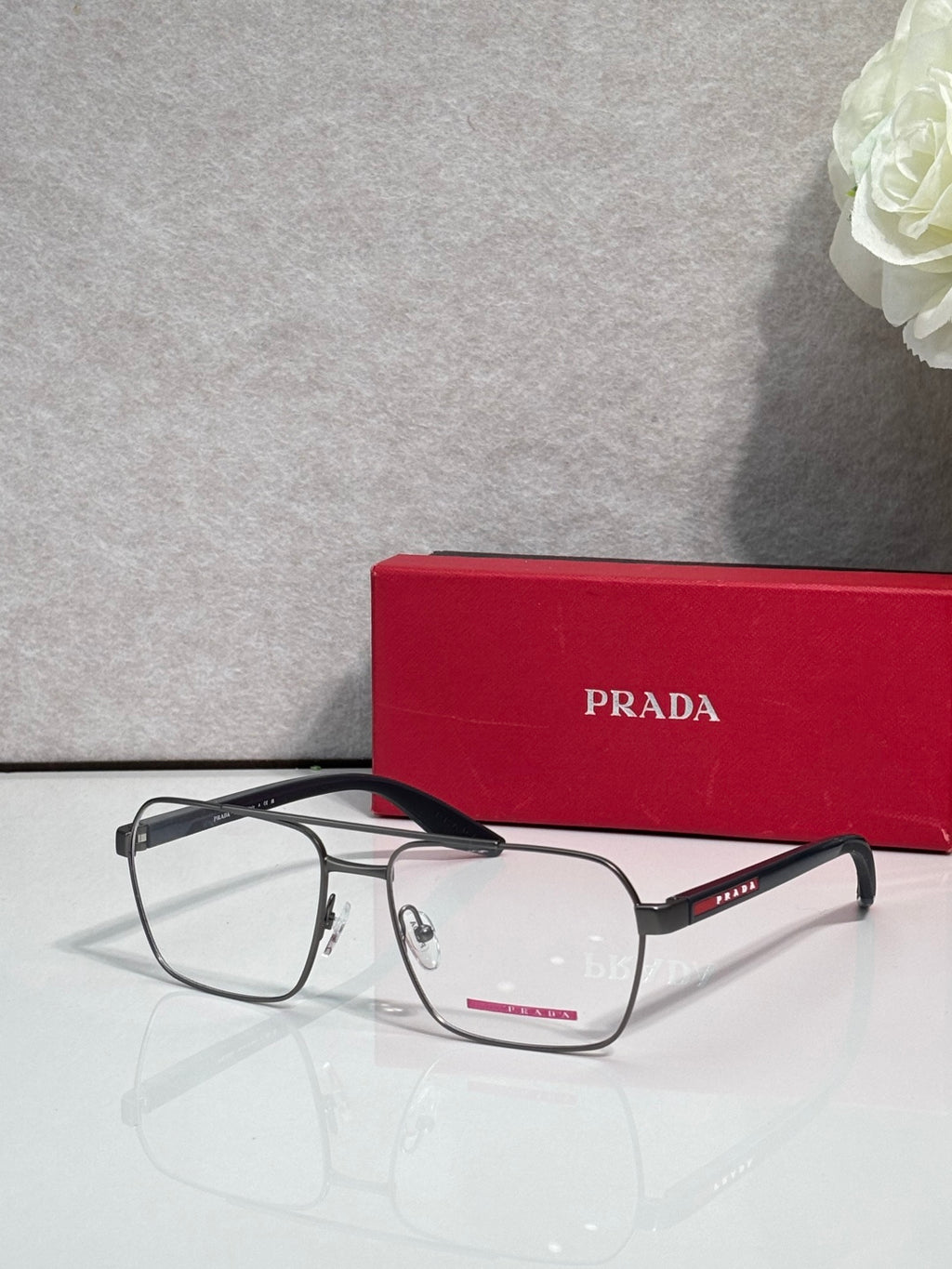 Prada eyeglasses with clear lenses and black frame, red temple logo strip at the side.