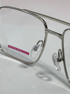 Prada eyeglasses close-up: clear lens and metal frame with small red logo detail.