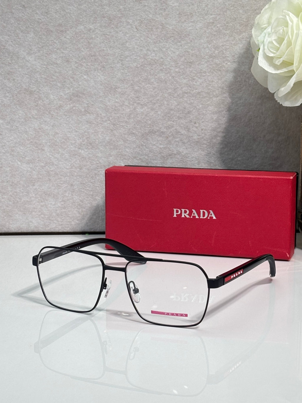 Prada eyeglasses with clear lenses and black rectangular frame, metal temple arms with logo.