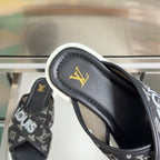 Louis Vuitton slide sandal, close-up of black leather strap and gold LV emblem.